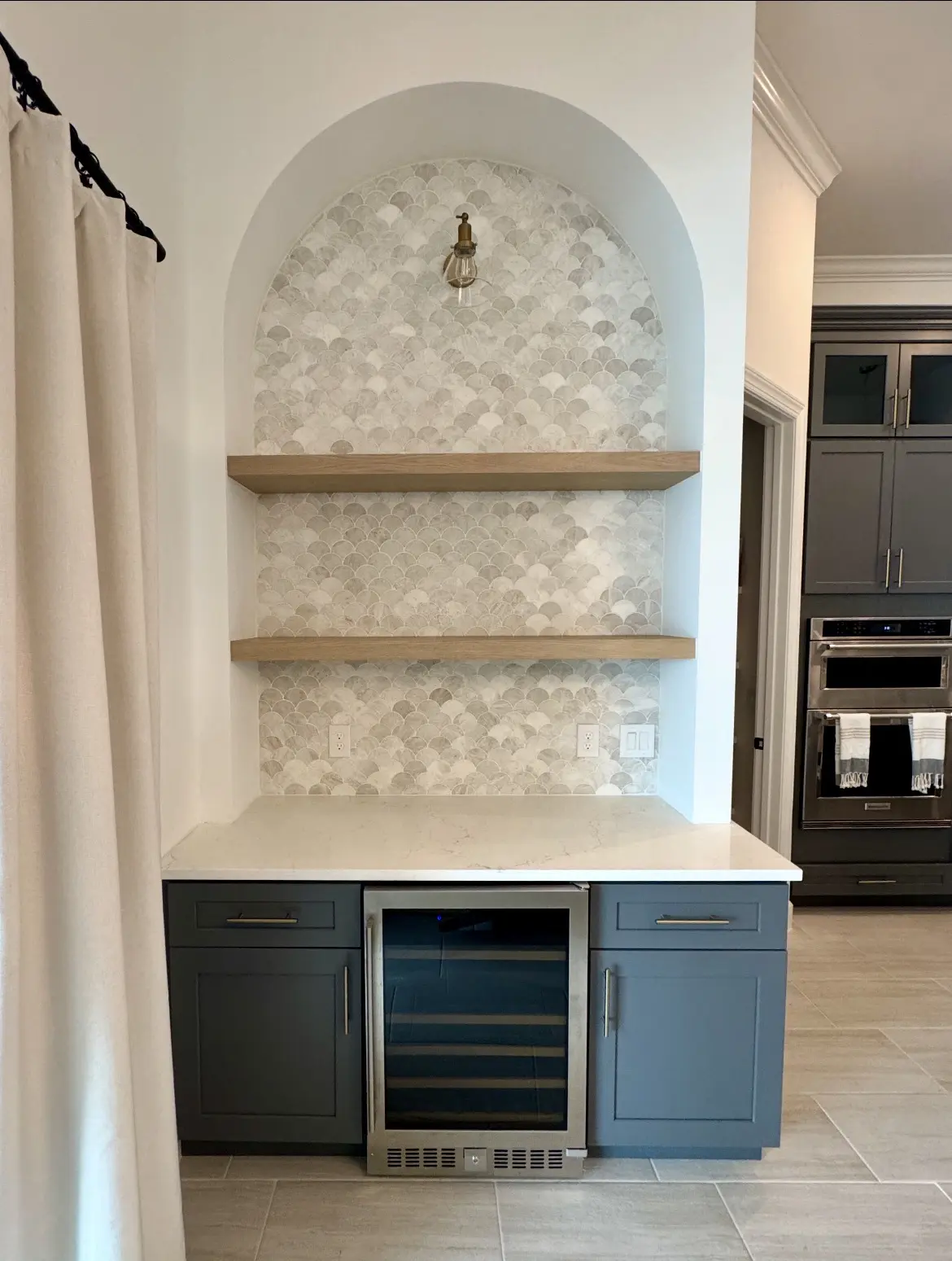 Custom arched beverage center with tile, floating shelves, cabinetry and wine refrigerator