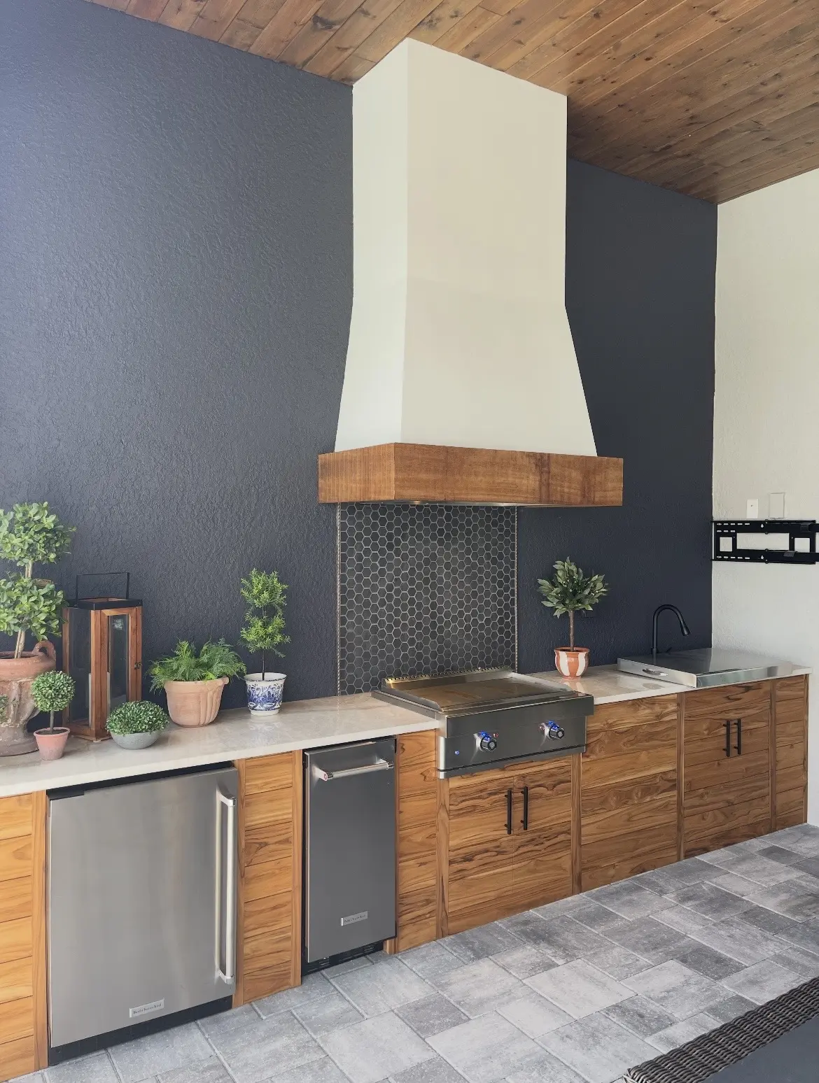 Completed custom site-built outdoor kitchen with wood-look cabinetry, griddle, sink and custom hood