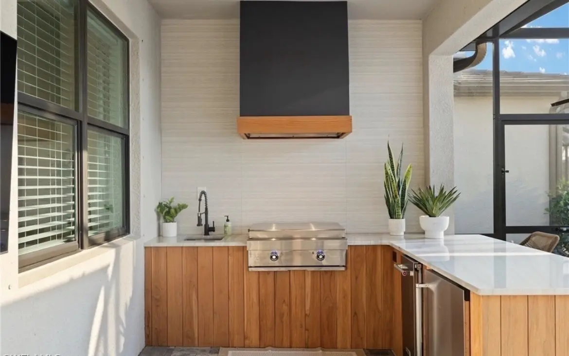 Completed custom site-built outdoor kitchen with warm wood-look finishes, grill, sink and peninsula